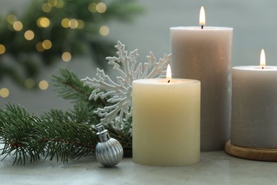 Photo of Burning candles, baubles and fir tree branches on white textured table, closeup