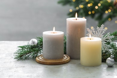 Photo of Burning candles, baubles and fir tree branches on white textured table, closeup