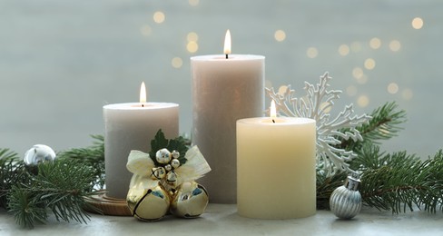 Photo of Burning candles, baubles and fir tree branches on white textured table, closeup