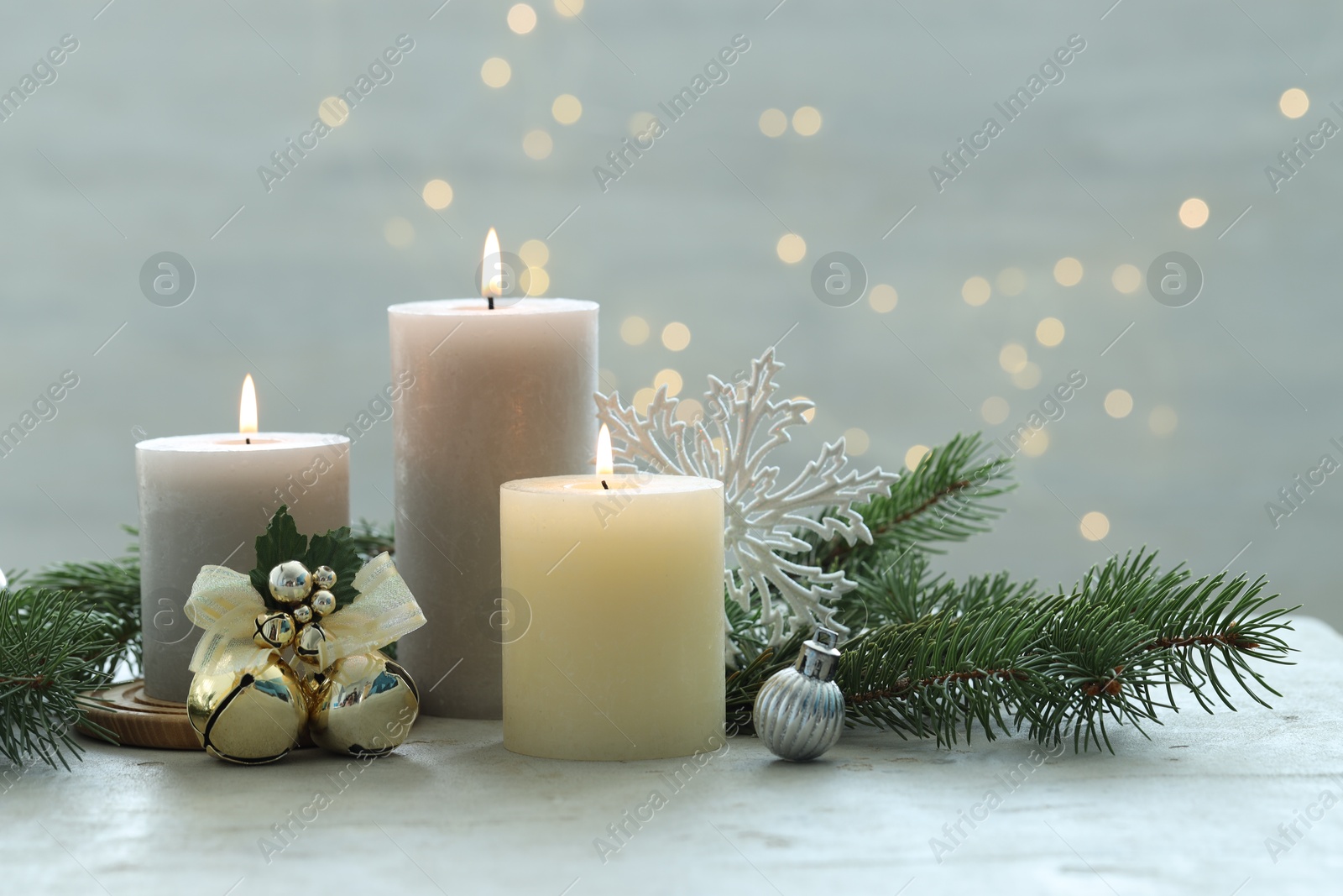 Photo of Burning candles, baubles and fir tree branches on white textured table, closeup