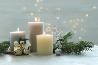 Photo of Burning candles, baubles and fir tree branches on white textured table, closeup