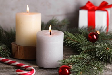 Photo of Burning candles, Christmas decor and fir tree branches on wooden table, closeup