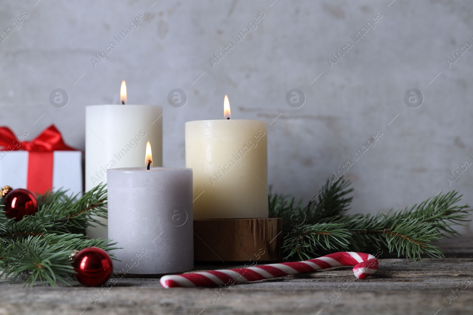 Photo of Burning candles, Christmas decor and fir tree branches on wooden table, closeup