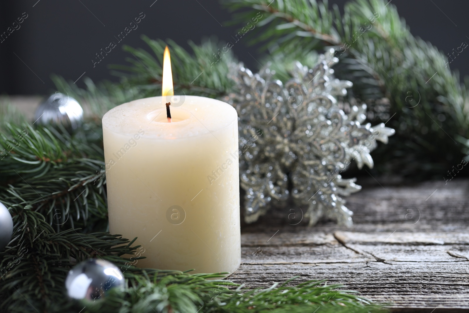 Photo of Burning candle, baubles and fir tree branches on wooden table, closeup. Space for text