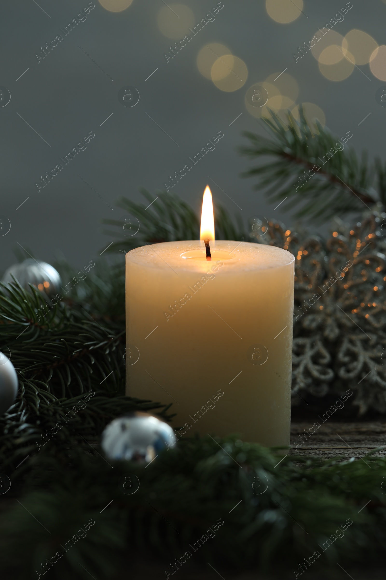 Photo of Burning candle, baubles and fir tree branches on wooden table, closeup