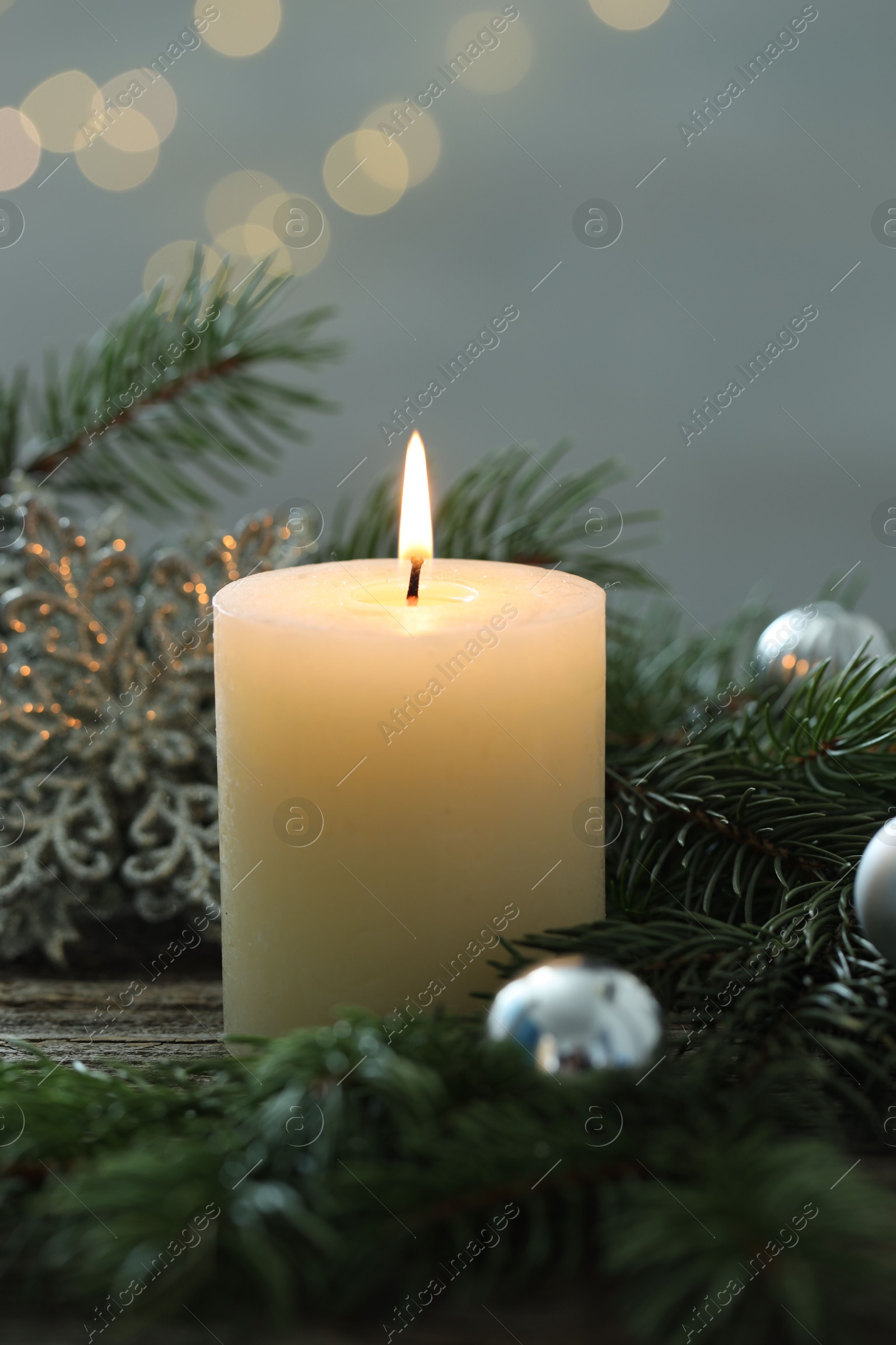 Photo of Burning candle, baubles and fir tree branches on wooden table, closeup