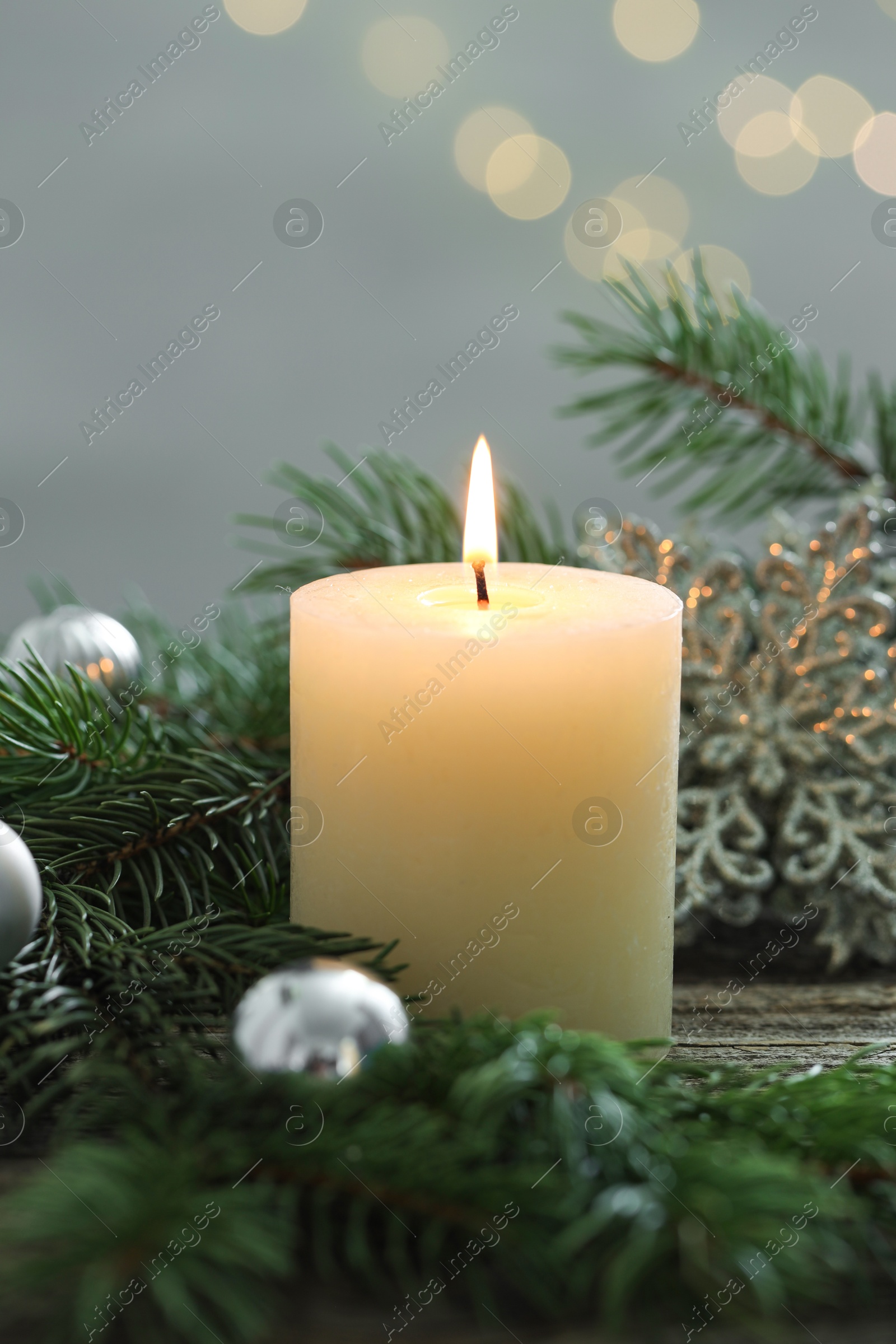 Photo of Burning candle, baubles and fir tree branches on wooden table, closeup