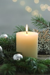 Photo of Burning candle, baubles and fir tree branches on wooden table, closeup