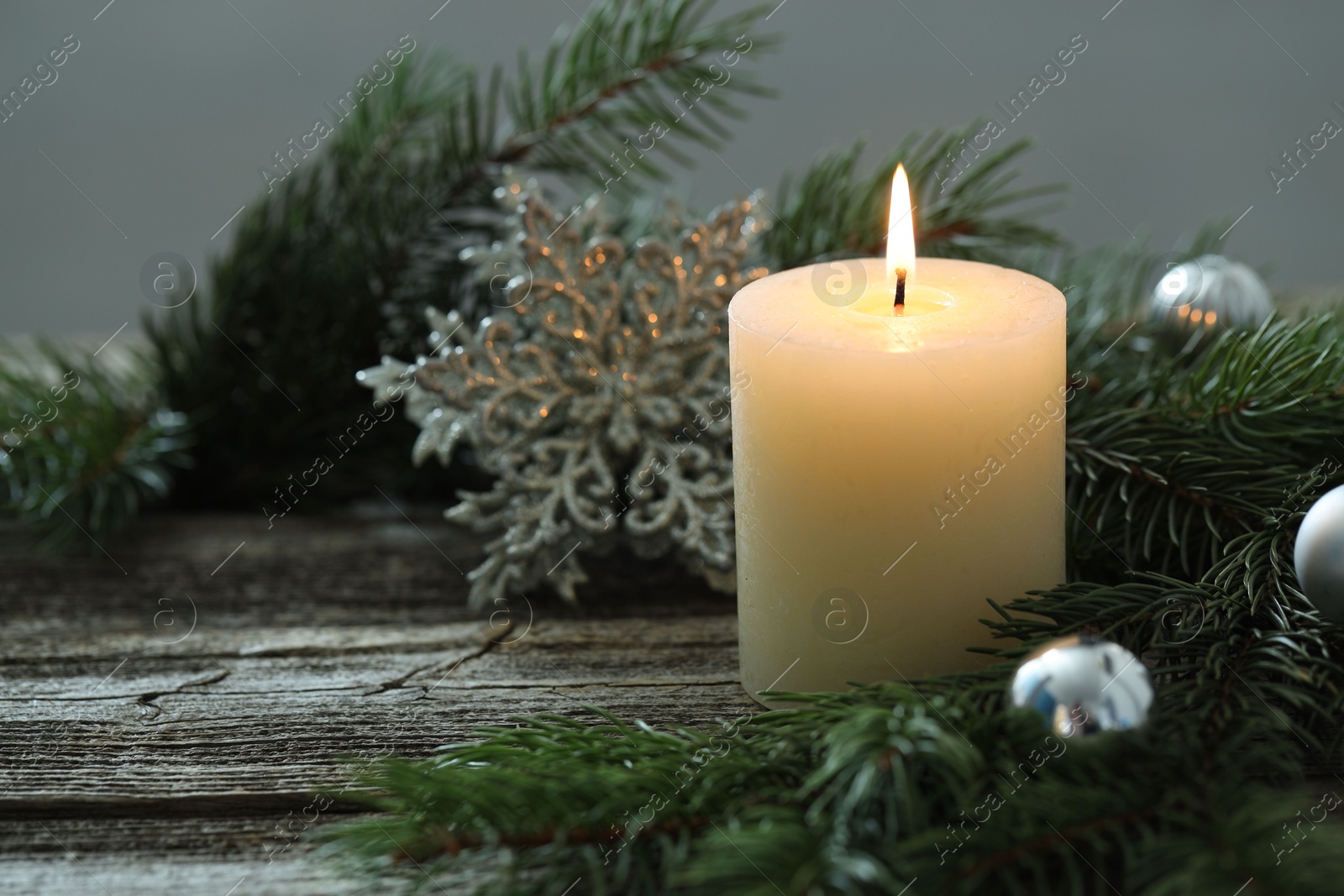 Photo of Burning candle, baubles and fir tree branches on wooden table, closeup. Space for text