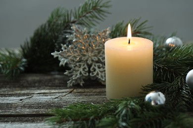 Photo of Burning candle, baubles and fir tree branches on wooden table, closeup. Space for text