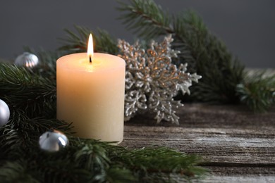 Photo of Burning candle, baubles and fir tree branches on wooden table, closeup. Space for text