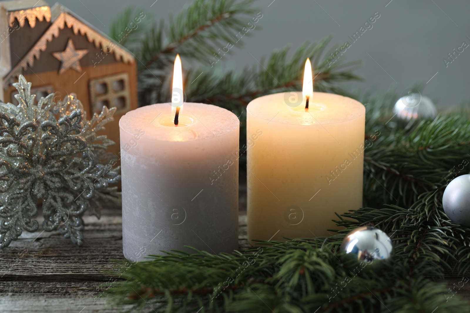 Photo of Burning candles, baubles and fir tree branches on wooden table, closeup