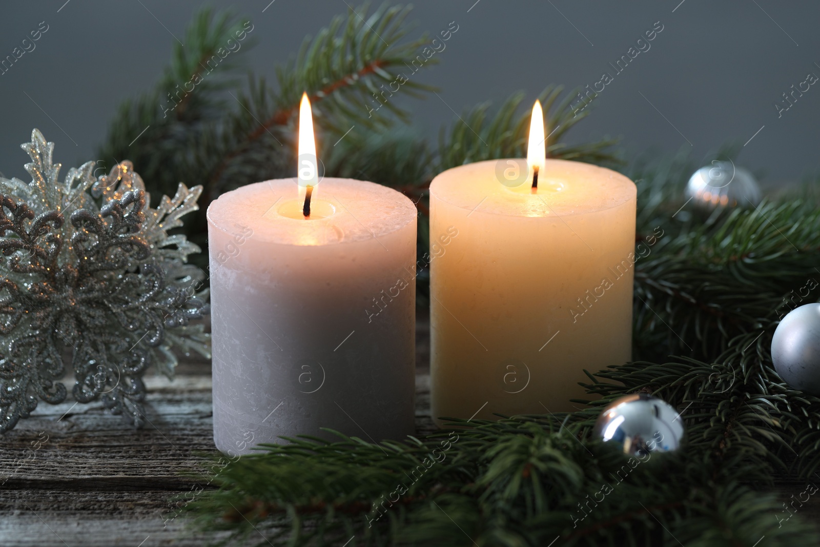 Photo of Burning candles, baubles and fir tree branches on wooden table, closeup