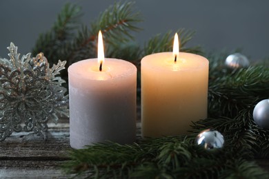 Photo of Burning candles, baubles and fir tree branches on wooden table, closeup