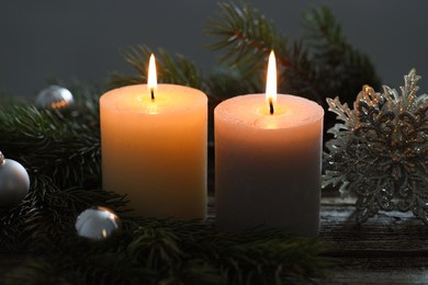 Photo of Burning candles, baubles and fir tree branches on wooden table, closeup