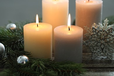 Photo of Burning candles, baubles and fir tree branches on wooden table, closeup