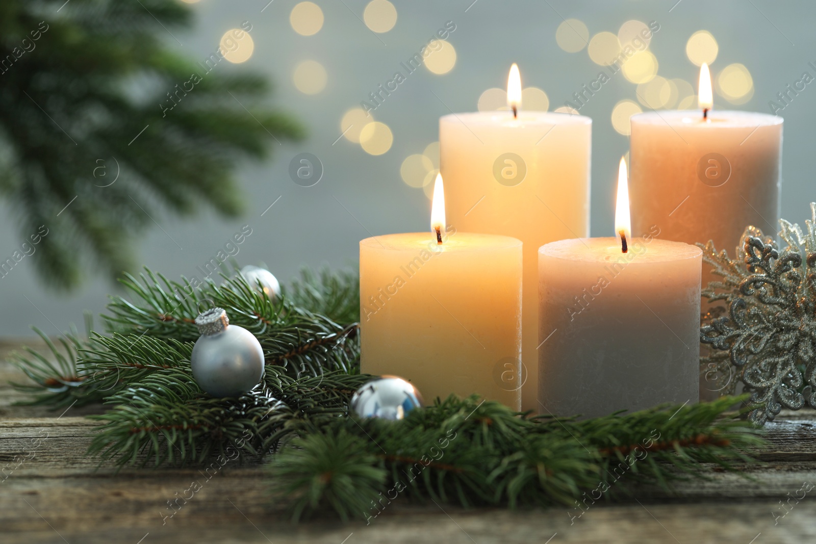 Photo of Burning candles, baubles and fir tree branches on wooden table, closeup