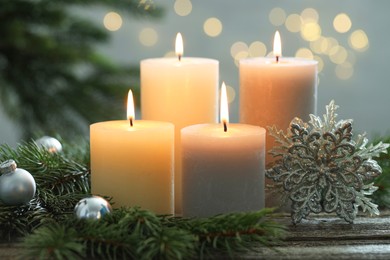 Photo of Burning candles, baubles and fir tree branches on wooden table, closeup