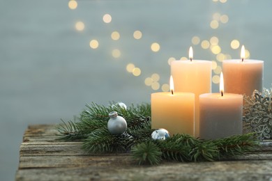 Photo of Burning candles, baubles and fir tree branches on wooden table, closeup. Space for text