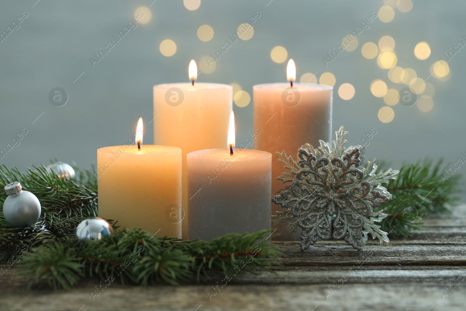 Photo of Burning candles, baubles and fir tree branches on wooden table, closeup