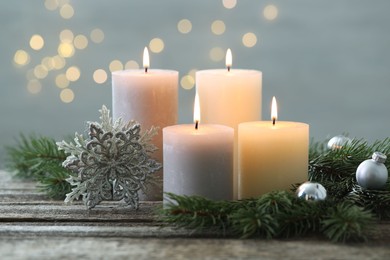 Photo of Burning candles, baubles and fir tree branches on wooden table, closeup