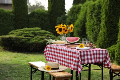 Fresh fruits, pie and vase with sunflowers on table in garden, space for text