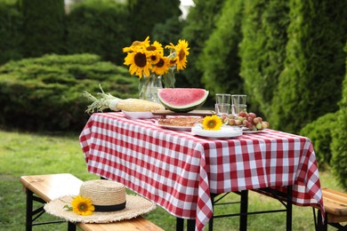 Fresh fruits, pie and vase with sunflowers on table in garden