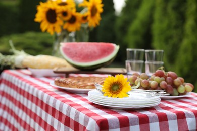 Fresh fruits, pie and vase with sunflowers on table in garden, closeup