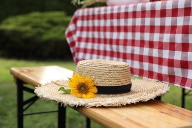 Straw hat with sunflower on wooden bench in garden, closeup