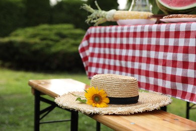 Straw hat with sunflower on wooden bench in garden, closeup