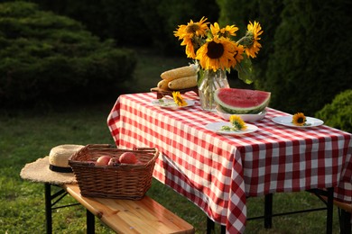 Vase of sunflowers, watermelon, corn and plates on table in garden