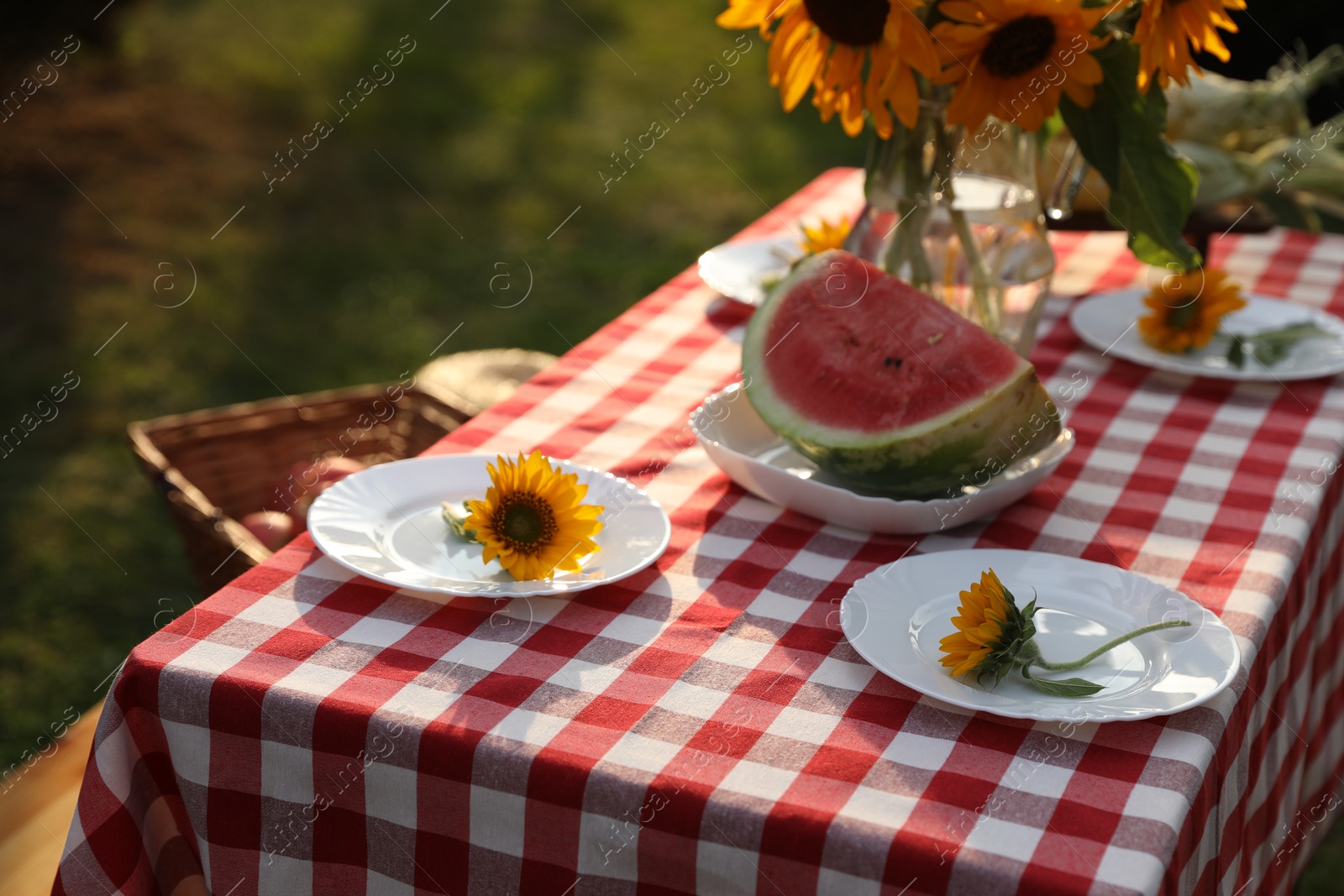 Photo of Plates with sunflowers and watermelon on table in garden