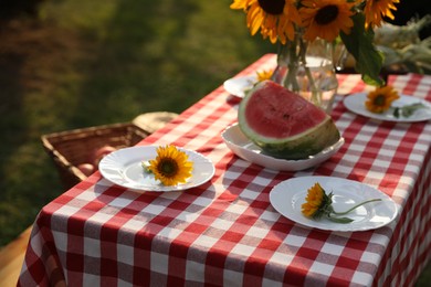 Photo of Plates with sunflowers and watermelon on table in garden