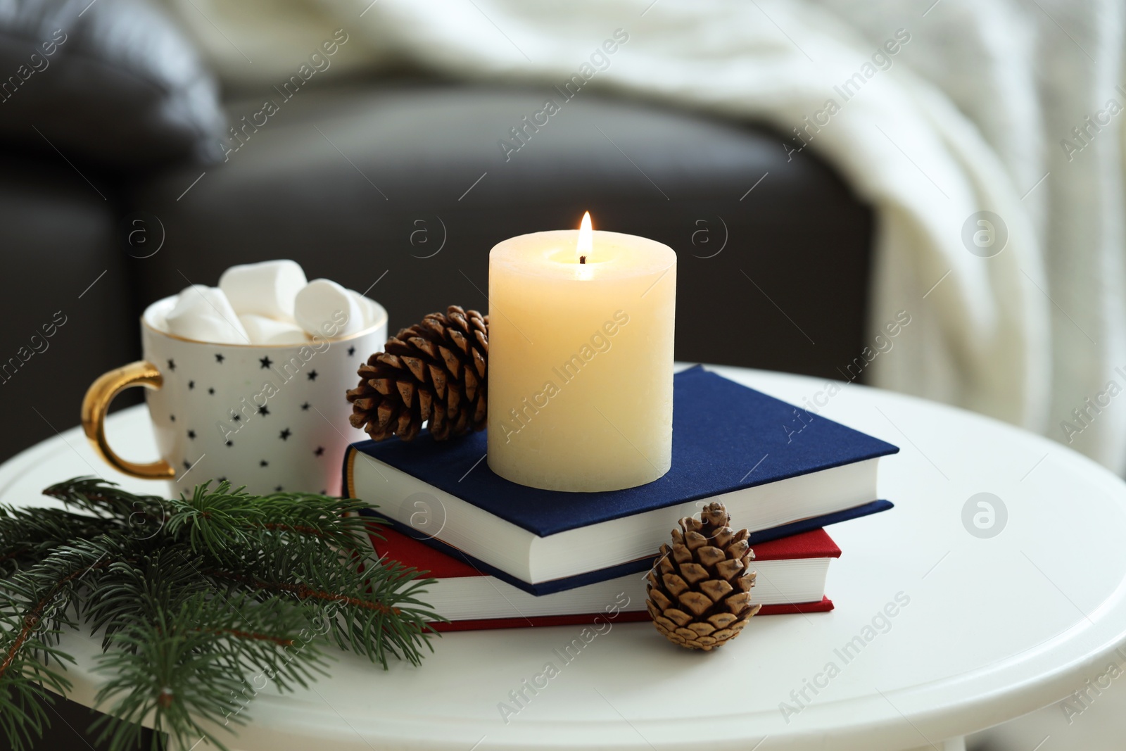 Photo of Burning candle, books, fir branches and cones on coffee table indoors. Christmas atmosphere