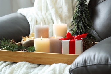 Photo of Tray with burning candles and Christmas decor on armchair