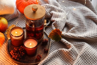 Photo of Burning candles, freshly brewed tea and autumn decor on fabric