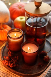 Photo of Burning candles, freshly brewed tea and autumn decor on fabric, closeup