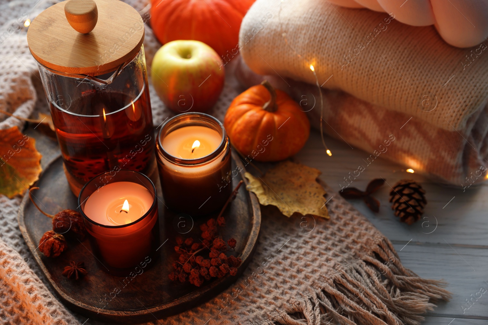 Photo of Burning candles, freshly brewed tea, sweaters and autumn decor on wooden table