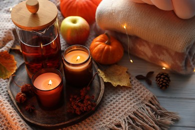 Photo of Burning candles, freshly brewed tea, sweaters and autumn decor on wooden table