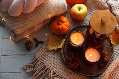 Photo of Burning candles, freshly brewed tea, sweaters and autumn decor on wooden table