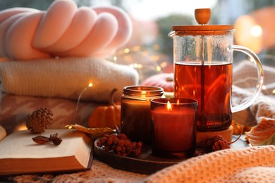 Photo of Burning candles, freshly brewed tea, sweaters, book and autumn decor on fabric