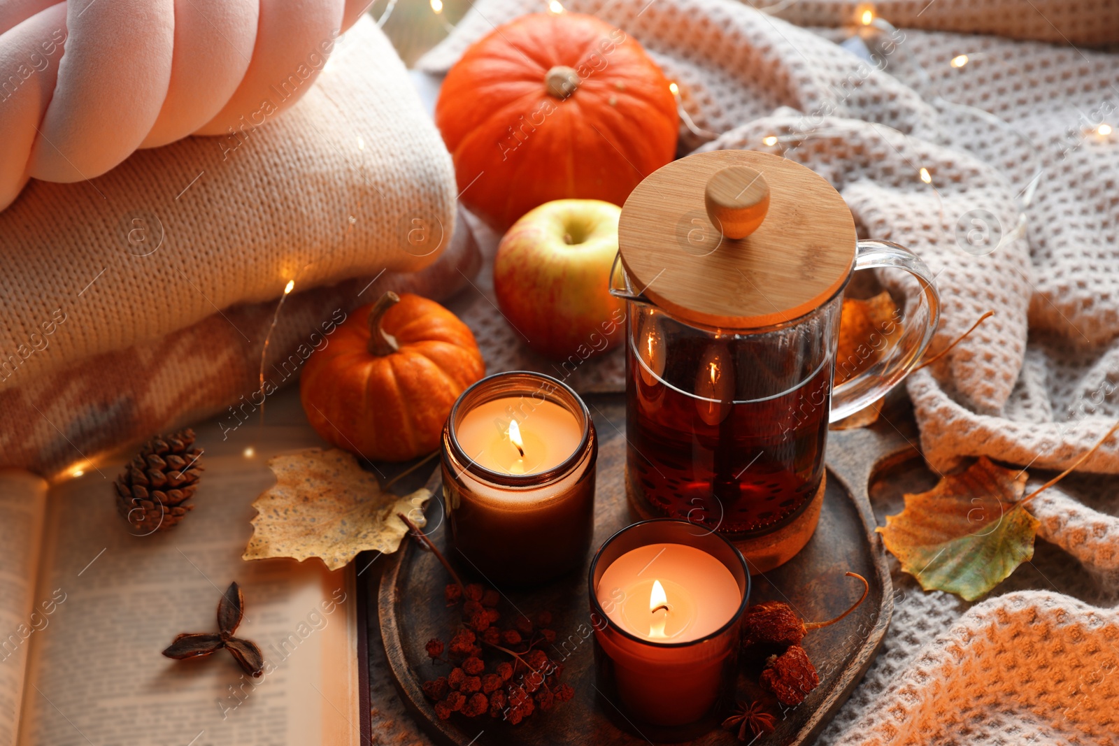 Photo of Burning candles, freshly brewed tea, sweaters, book and autumn decor on fabric