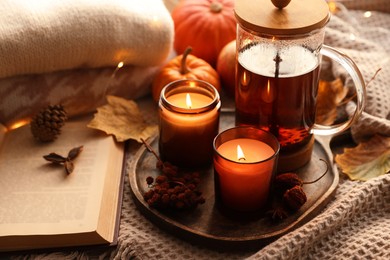 Photo of Burning candles, freshly brewed tea, sweaters, book and autumn decor on fabric