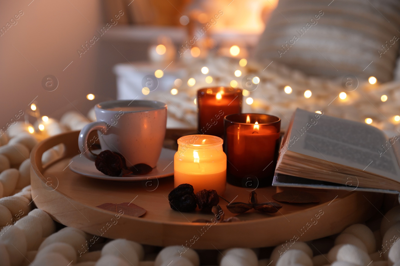 Photo of Burning candles, lights, coffee, book and decor on bed indoors, closeup. Autumn atmosphere