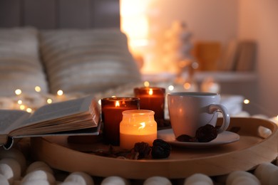 Photo of Burning candles, lights, coffee, book and decor on bed indoors, closeup. Autumn atmosphere