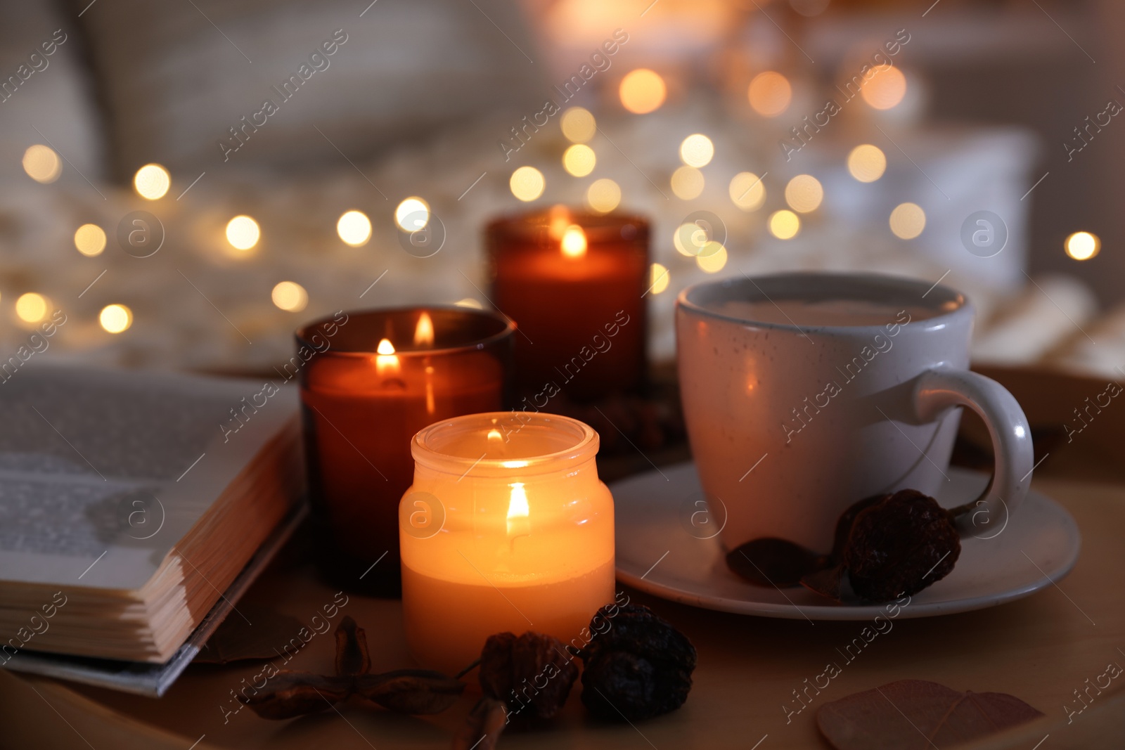 Photo of Burning candles, lights, coffee, book and decor on bed indoors, closeup. Autumn atmosphere