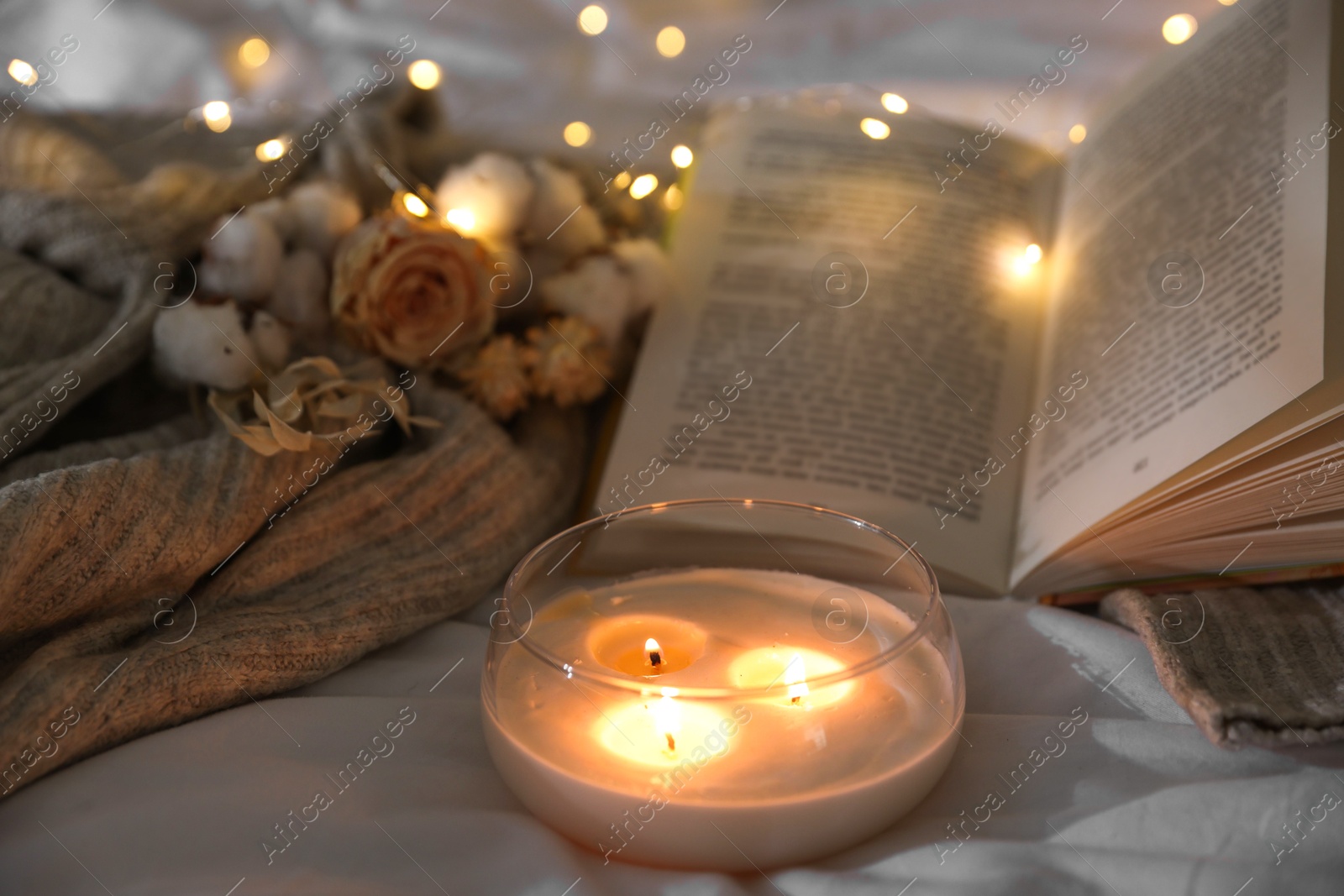 Photo of Burning candle, book, sweater and dry flowers on white cloth, closeup. Autumn aesthetics