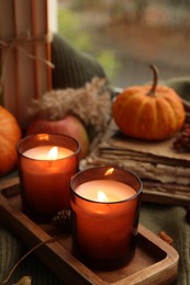 Photo of Burning candles, books and autumn decor on green sweater near window, closeup