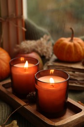 Photo of Burning candles, books and autumn decor on sweater near window, closeup