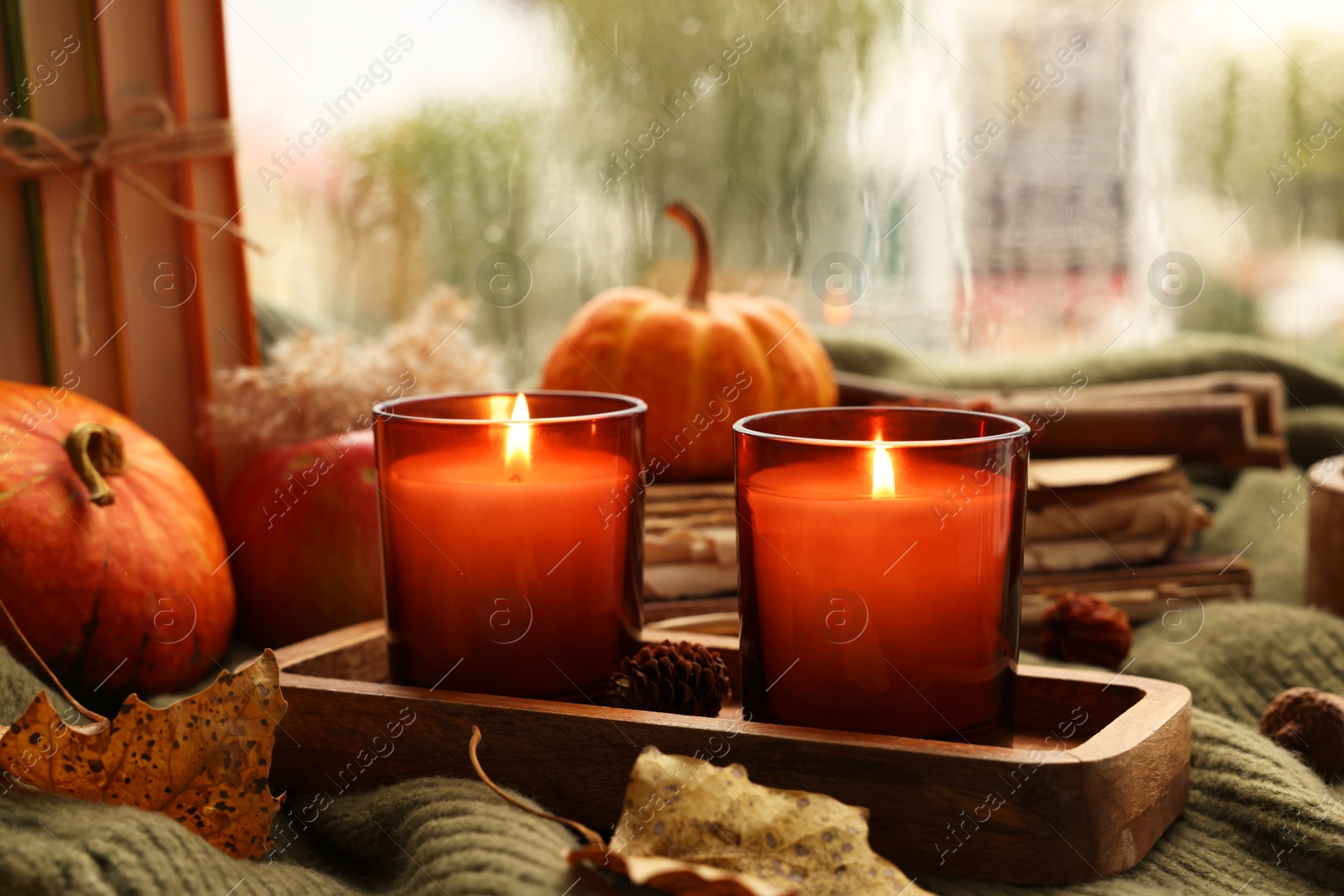 Photo of Burning candles and autumn decor on green sweater near window